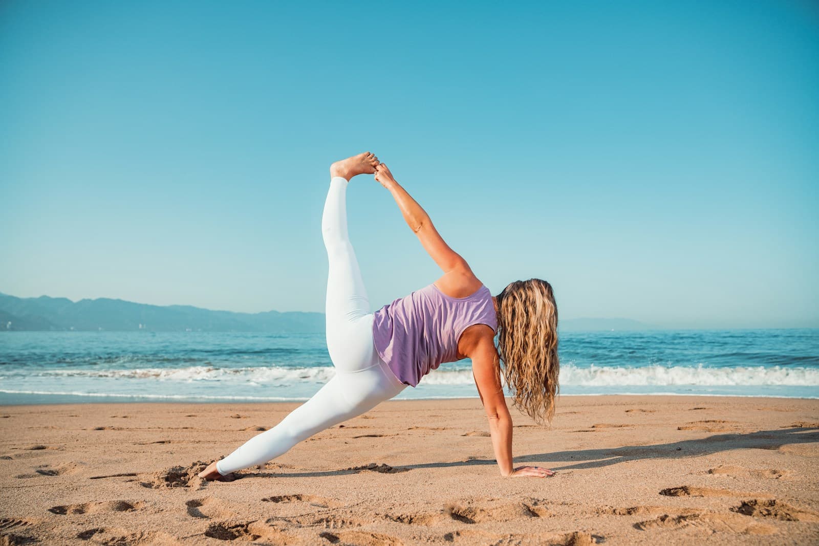 A person practising yoga on a sunny beach beside the sea.