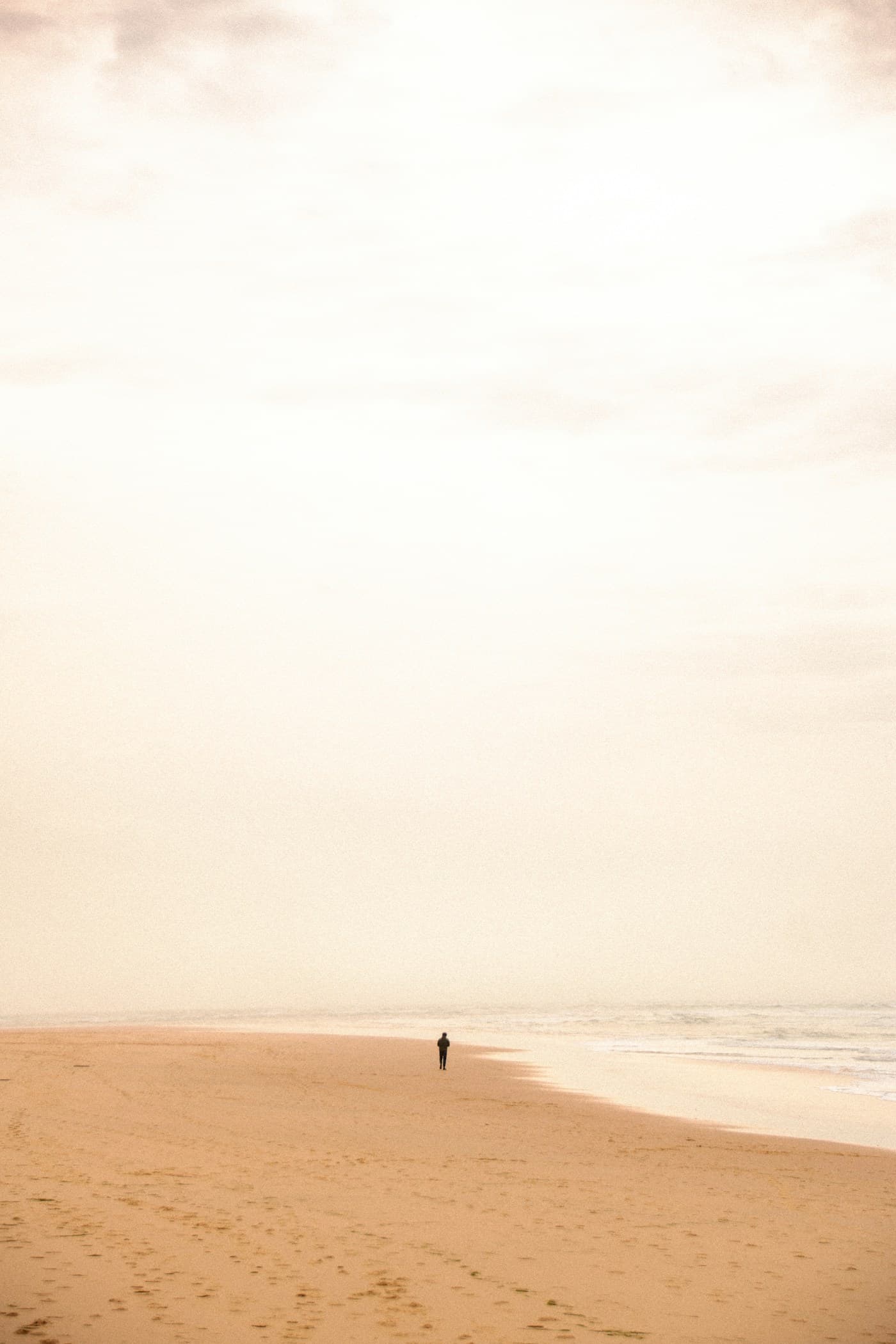 A distant person walking along a quiet sandy beach.
